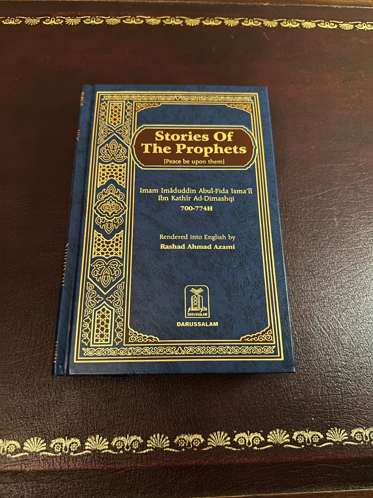 Blue and gold Darussalam hardback cover of Stories of the Prophets by Ibn Kathir, photographed on a brown leather desk.