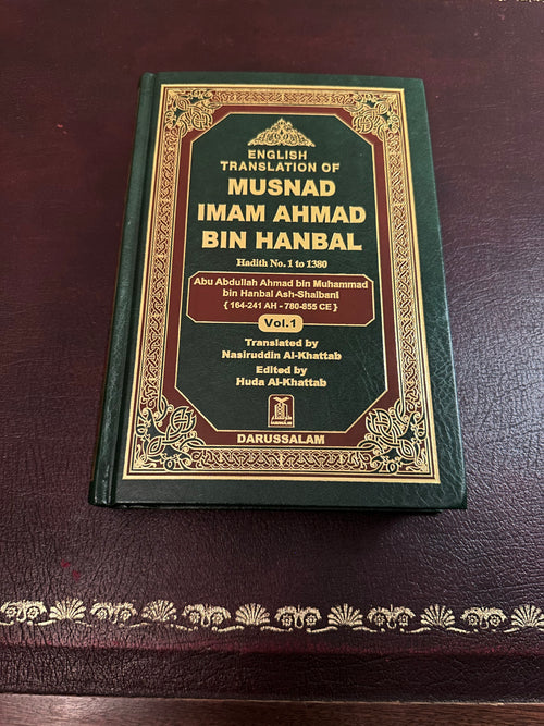 Green-and-gold Darussalam hardback cover of Musnad Imam Ahmad, Volume 1, photographed on a brown leather desk.