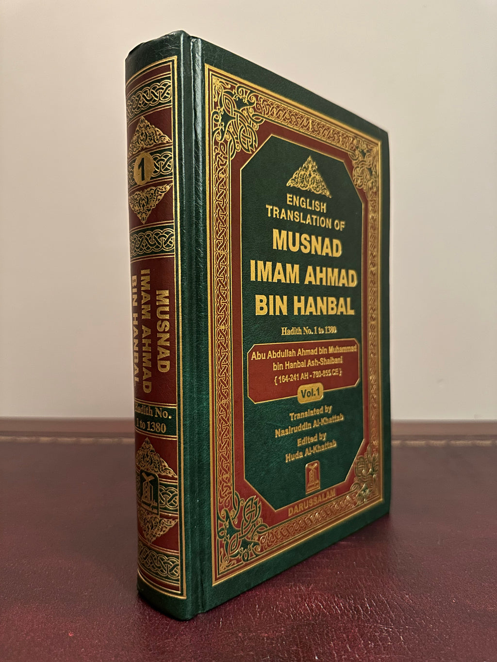 Angled view of the green-and-gold Darussalam Musnad Imam Ahmad Volume 1 hardback, showing its spine and front cover on a brown leather desk.