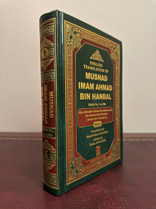 Angled view of the green-and-gold Darussalam Musnad Imam Ahmad Volume 1 hardback, showing its spine and front cover on a brown leather desk.